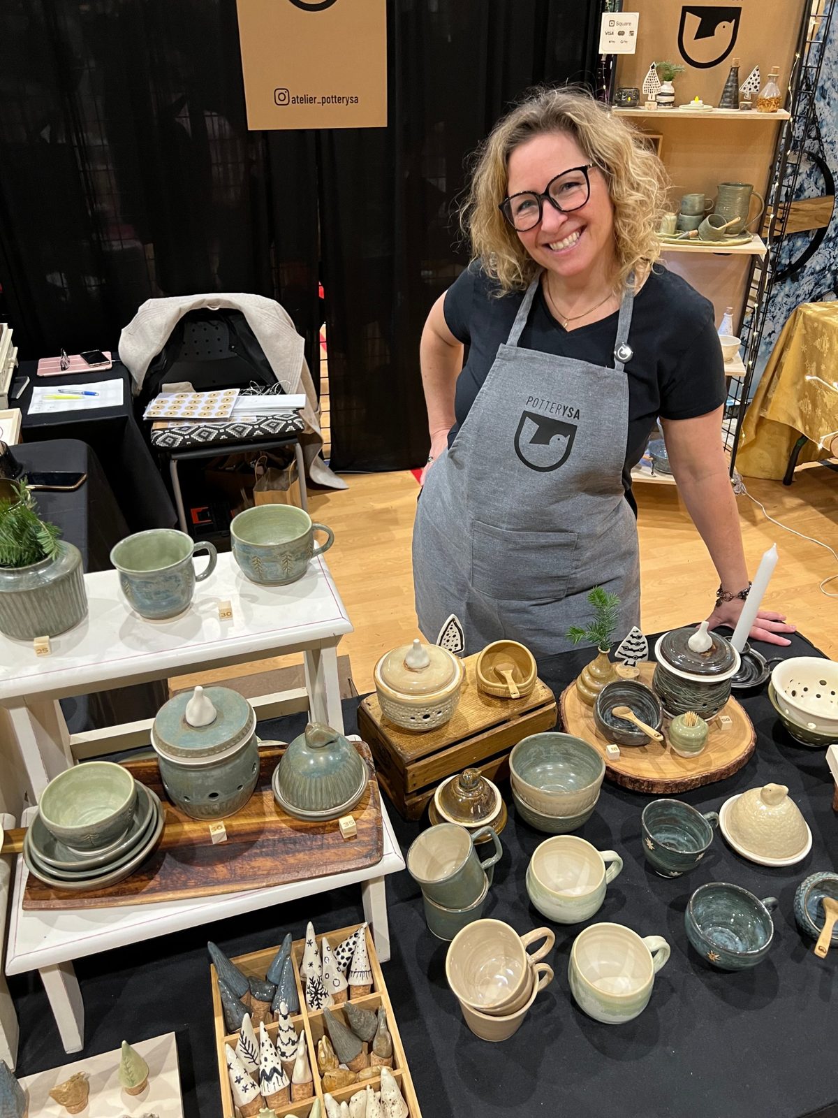 Ysabel, tout sourire, derrière sa table de poterie dans un marché de Noël